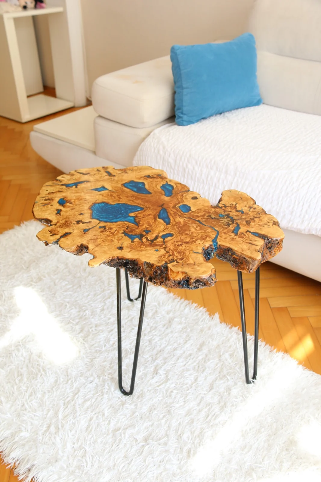 Olive wood coffee table on slender black hairpin legs beside a white sofa