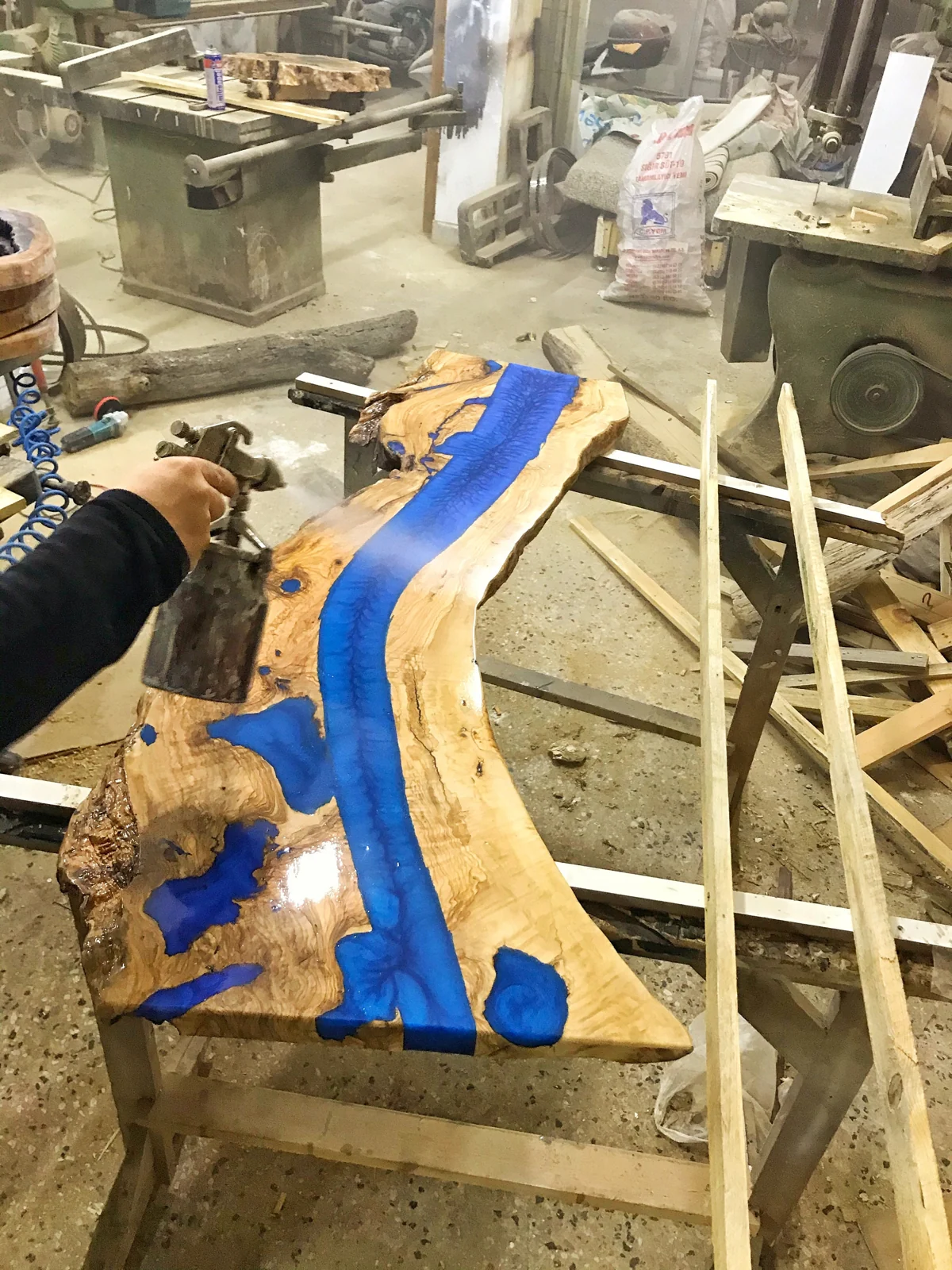 Craftsperson finishing the olive wood blue epoxy tabletop in the workshop