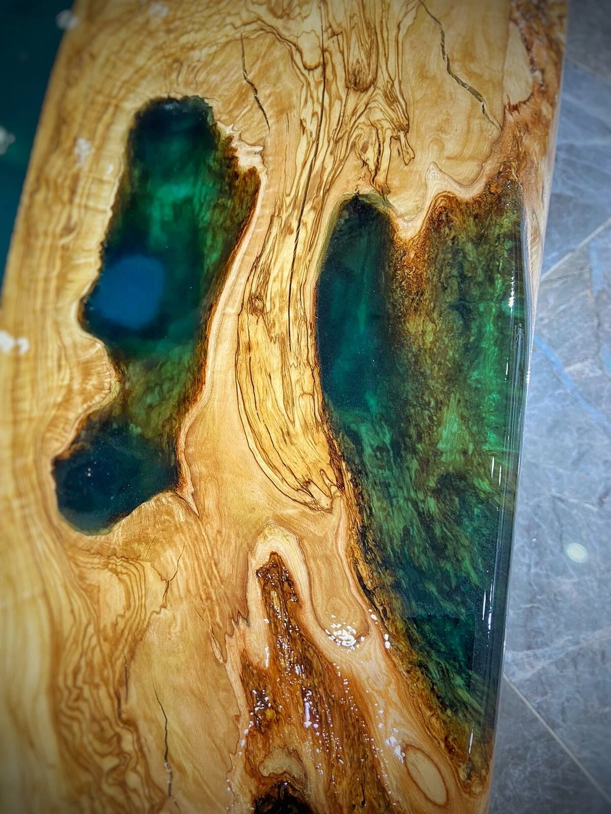 Close view of blue-green epoxy accents within natural olive wood openings
