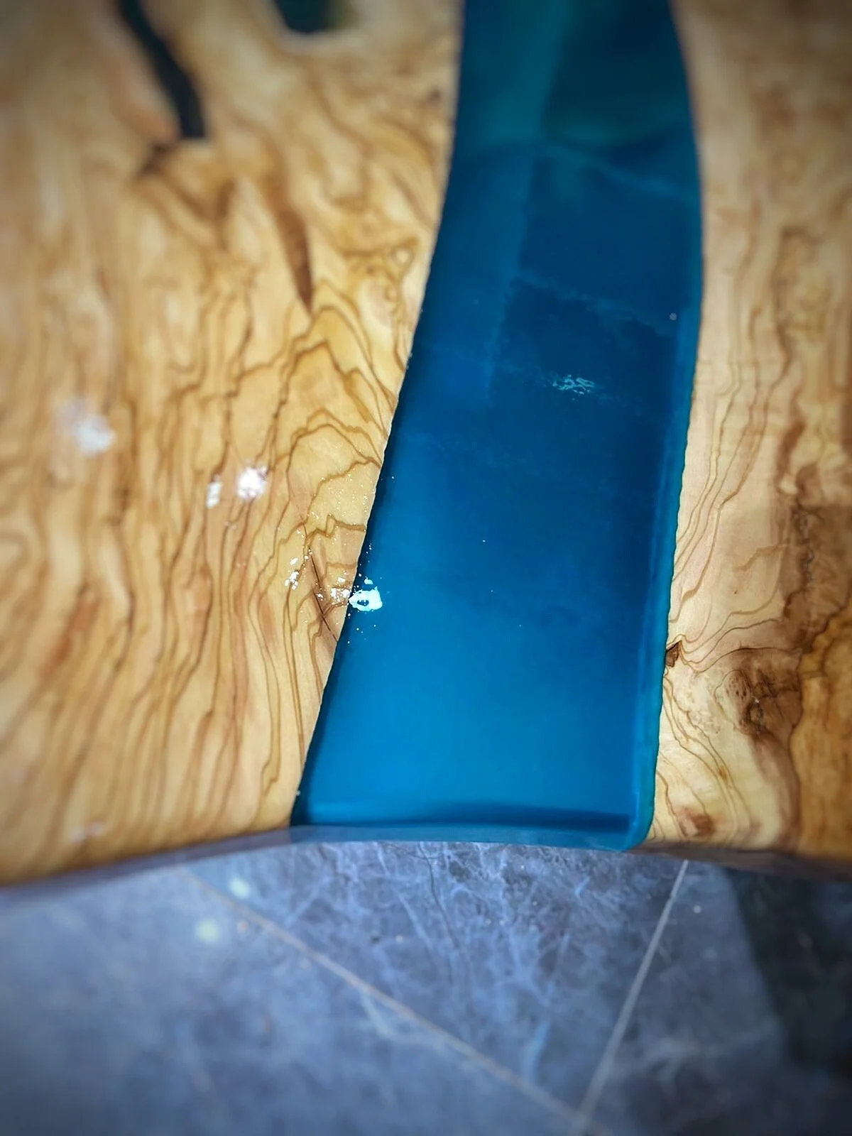 Detail of the blue resin channel beside golden olive wood grain