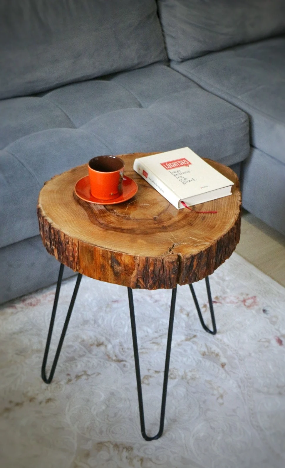 Round walnut wood slice coffee table with a bark edge and black hairpin legs beside a grey sofa