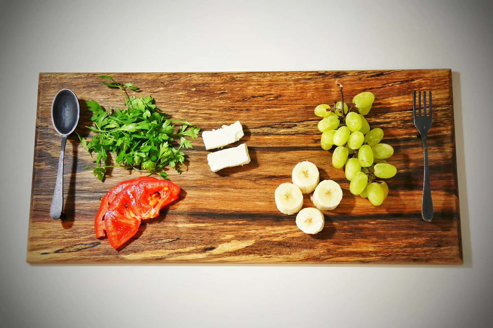 Top view of a walnut serving board arranged with cheese, grapes and vegetables