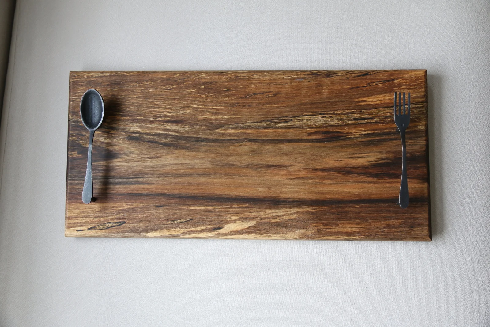 Walnut serving board without handles showing natural grain and a spoon and fork