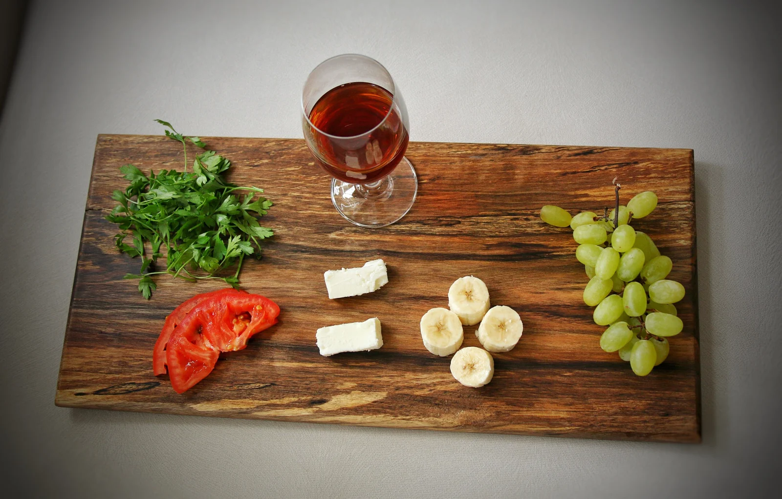 Overhead walnut serving tray with wine, cheese, grapes and fresh herbs